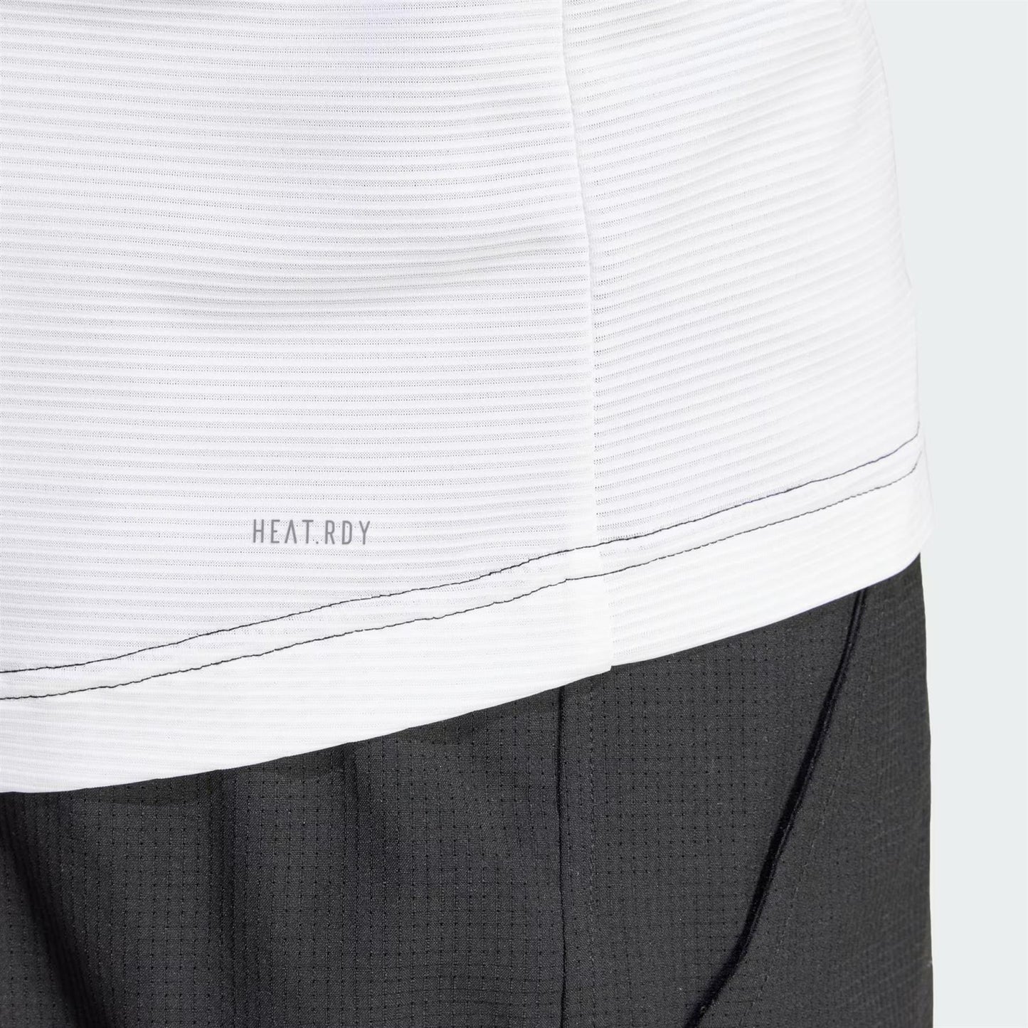 Close-up of an adidas Men's Pro Freelift 3D Badminton T-Shirt in black and white, featuring "HEAT.RDY" branding, paired with black bottoms. The shirt displays a textured, ribbed pattern while the grid-like texture on the bottoms complements the sophisticated style.