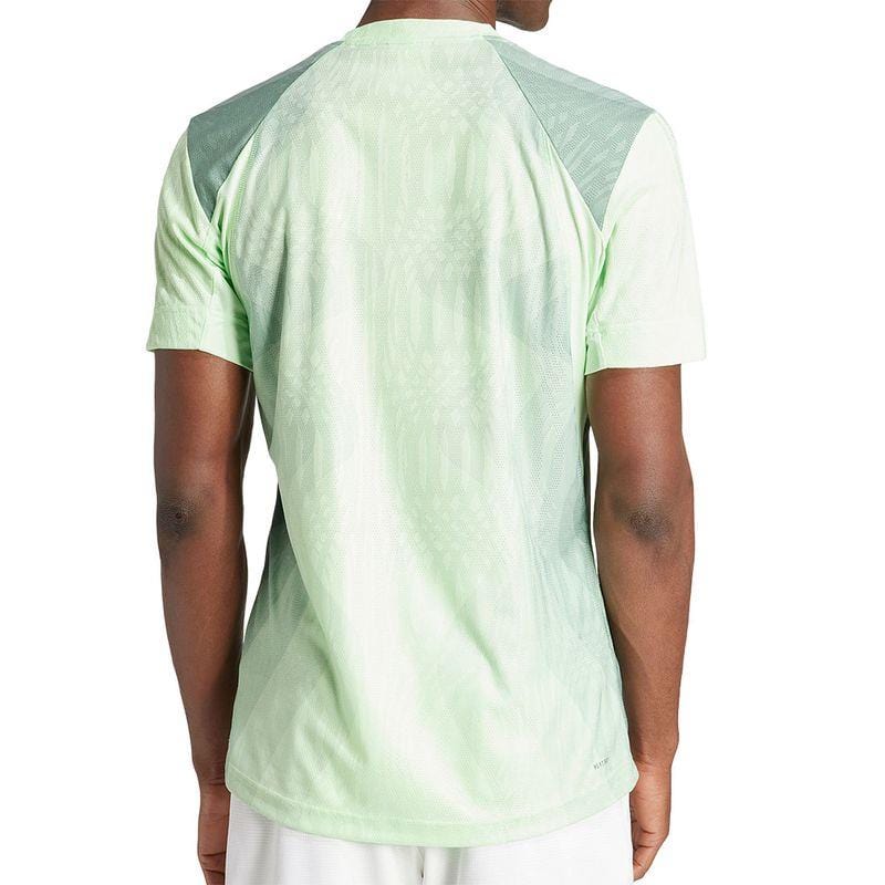 The individual is wearing the adidas Melbourne Men's Pro Badminton T-Shirt in green, crafted from recycled polyester. It showcases a light green design with darker green on the shoulders, ensuring optimal comfort. When paired with white shorts, it provides a sporty yet stylish appearance.