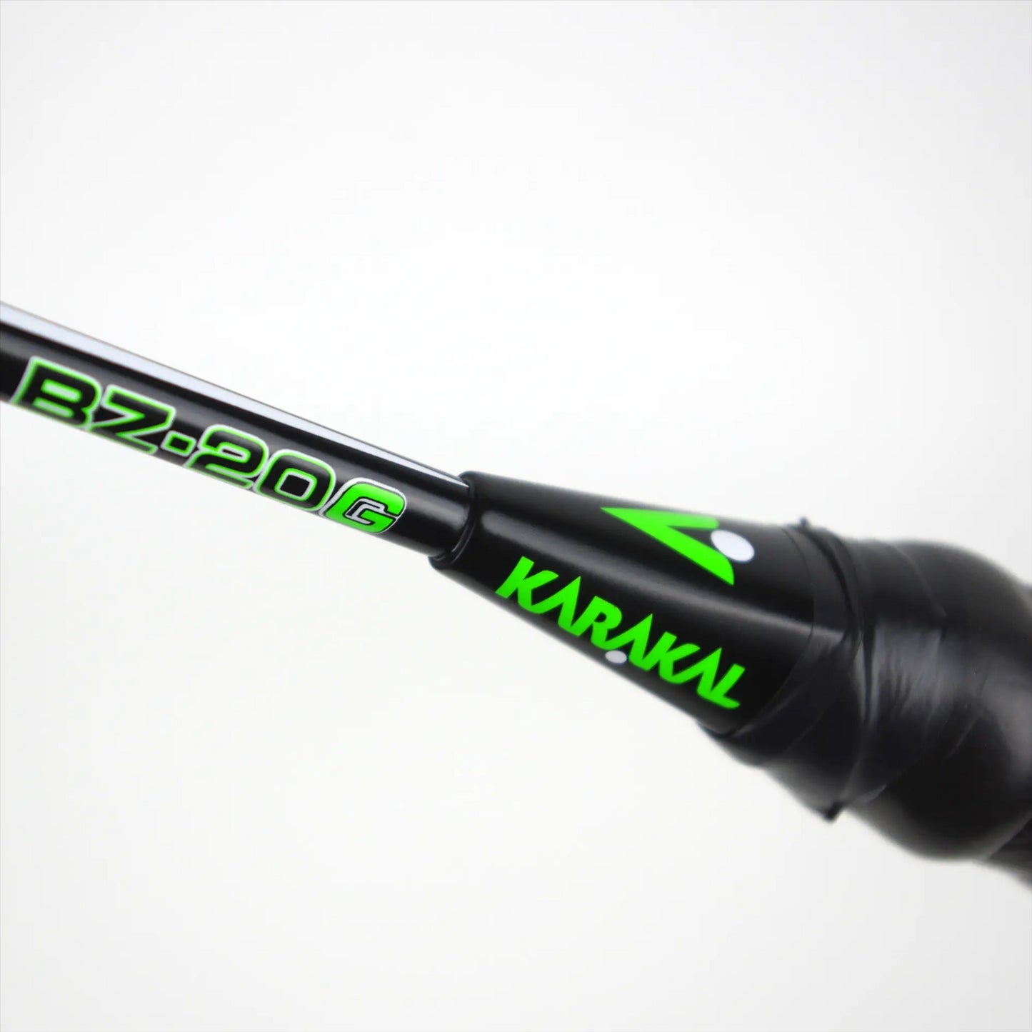 A close-up view of the Karakal BZ 20 2.1 badminton racket showcases the shaft with "Karakal" branding and the model number "BZ-20 G" in green lettering set against a white background. The isometric head is designed for enhanced performance, and the handle is wrapped in black PU Super Grip tape to ensure superior control.