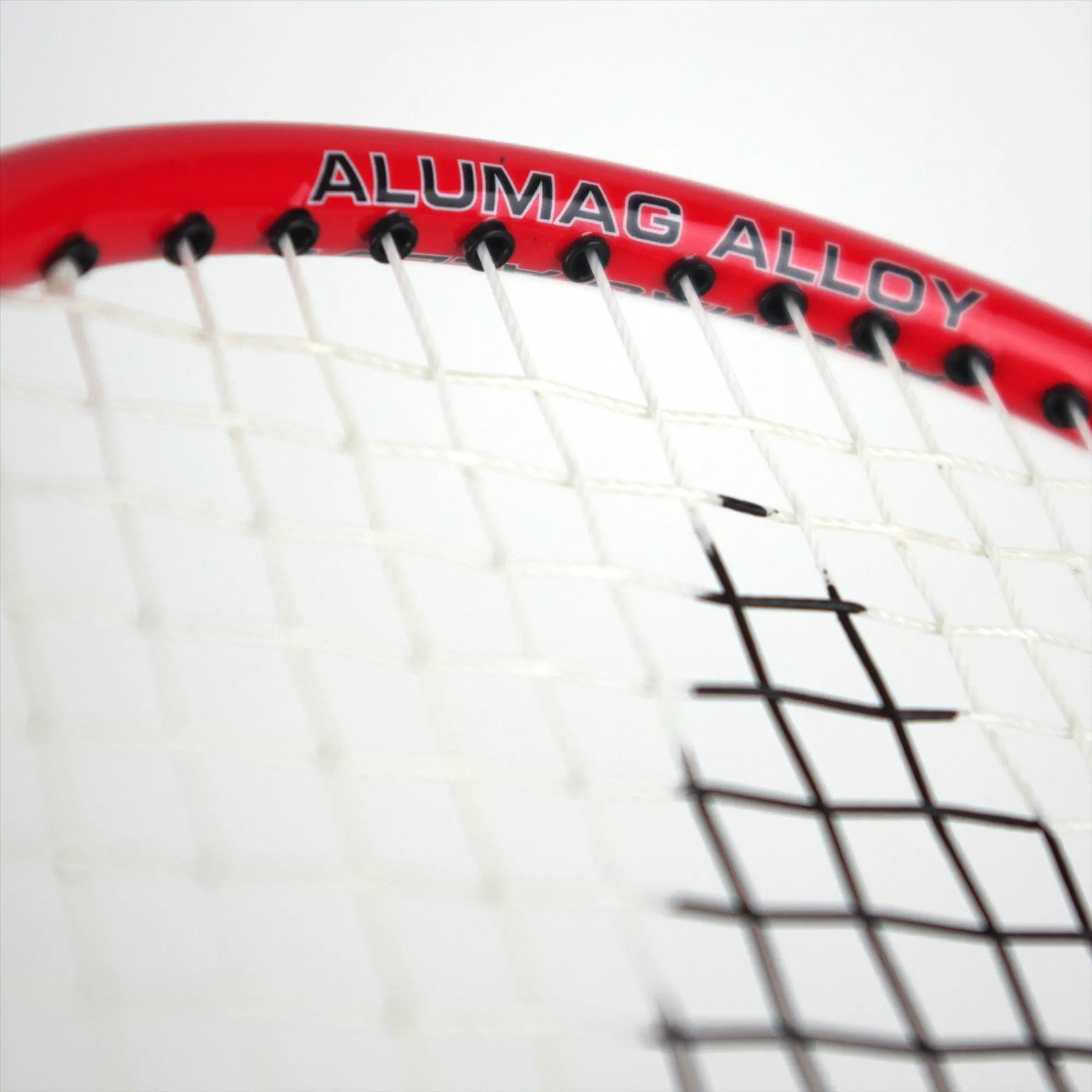 Close-up of the Karakal CB-2 2.1 Junior Badminton Racket's isometric head featuring a red frame and white strings. The words "Alumag Alloy" are printed in black on the aluminium frame, highlighting the string pattern and construction of this striking Karakal racket.