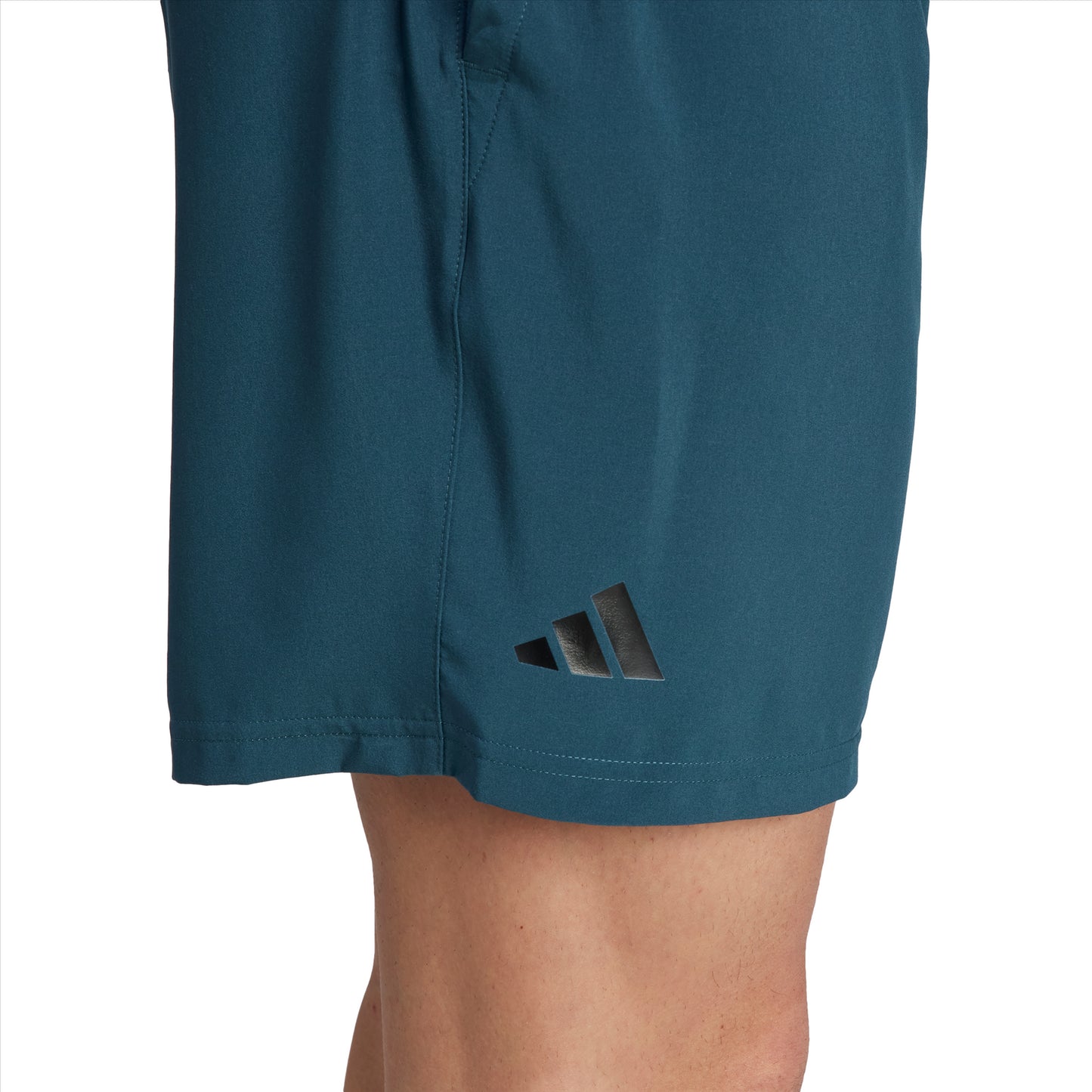 Close-up of a person wearing green adidas Club Stretch Woven 7" Men's Badminton Shorts, showcasing a subtle black logo with three diagonal stripes on the left side. These shorts are designed with AEROREADY technology. The person's leg is partially visible, exhibiting a beige skin tone.