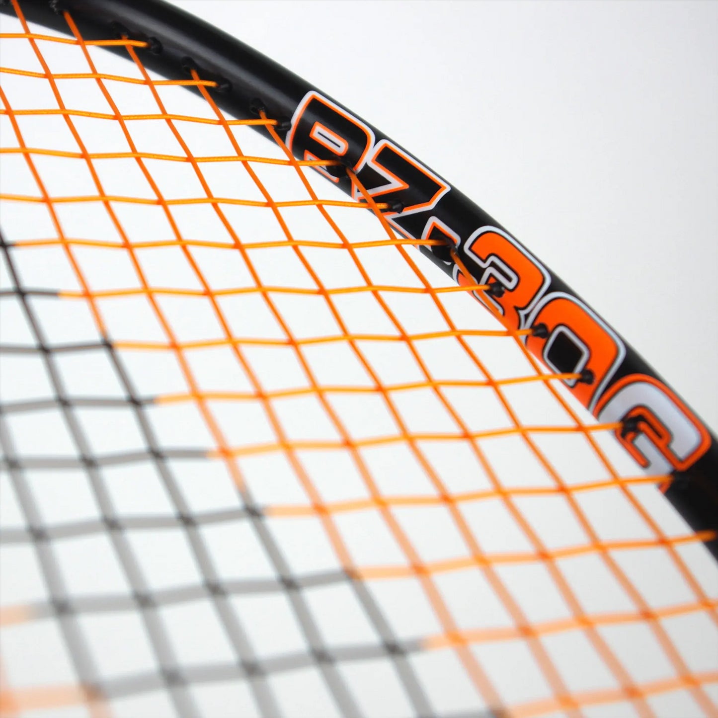 Close-up of a Karakal badminton racket with an orange and black frame featuring a crisscrossing orange string pattern, reminiscent of an isometric head. The handle displays the text "BZ 30 2.1." The background is a blurred white.