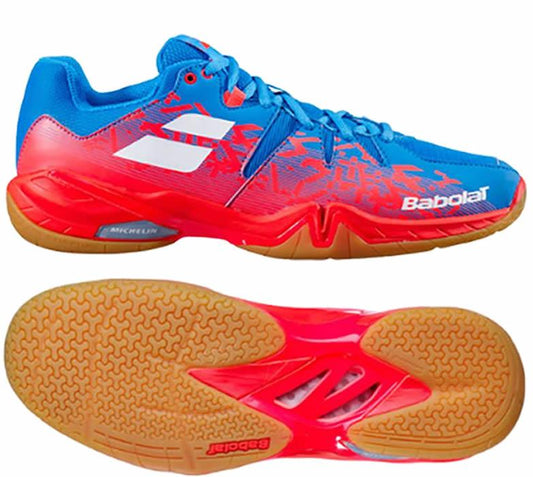 The Babolat Shadow Spirit Badminton Shoes in Blue Red boast a vibrant design with blue and red hues complemented by white accents. They are crafted with a textured Michelin rubber sole for excellent grip and prominently feature the Babolat brand logo on the sides and sole, ensuring style meets performance.