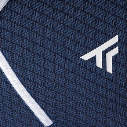 Close-up of a patterned fabric with a geometric design in navy and light blue. The Tecnifibre Mens Thermo Badminton Zipper Longsleeve, featuring a zipper that runs smoothly along the left edge, complements the prominent white logo resembling stylized letters or arrows.