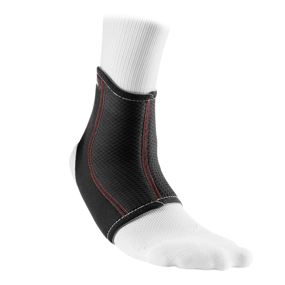 A close-up of an ankle wearing a white sock with the McDavid Ankle Sleeve, a black neoprene brace featuring red stitching and a textured surface for optimal support and compression therapy. This sleeve extends from the ankle to just above the foot, ensuring comfort and stability.