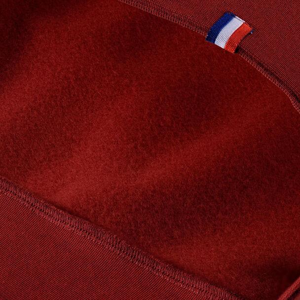 Close-up of the cardinal fabric with a small blue, white, and red striped tag at the seam, showcasing texture and stitching detail. The cotton fleece lends a high-performance look reminiscent of the Tecnifibre Men's Team Badminton Sweater by Tecnifibre.