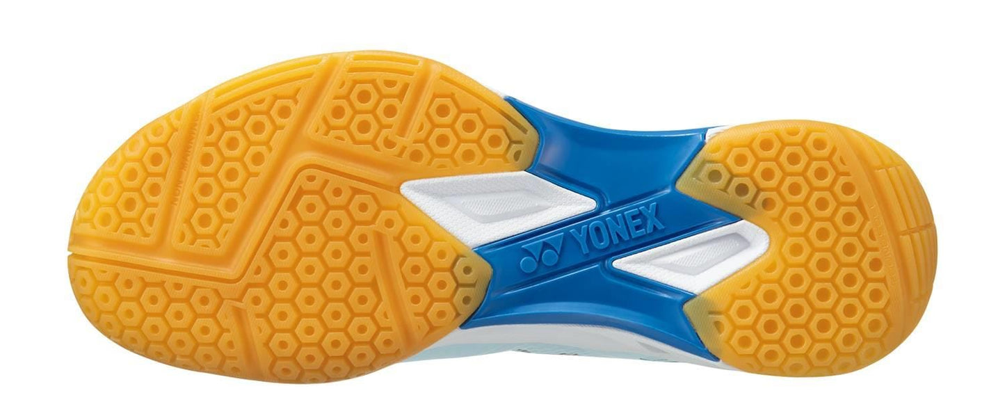 A close-up of a Yonex Power Cushion Eclipsion X3 sole reveals a honeycomb pattern in vibrant yellow, complemented by touches of blue and white. The "Yonex" brand name is prominently displayed on the arch area, amidst dynamic color contrasts and geometric designs, making it ideal for badminton or indoor court play.