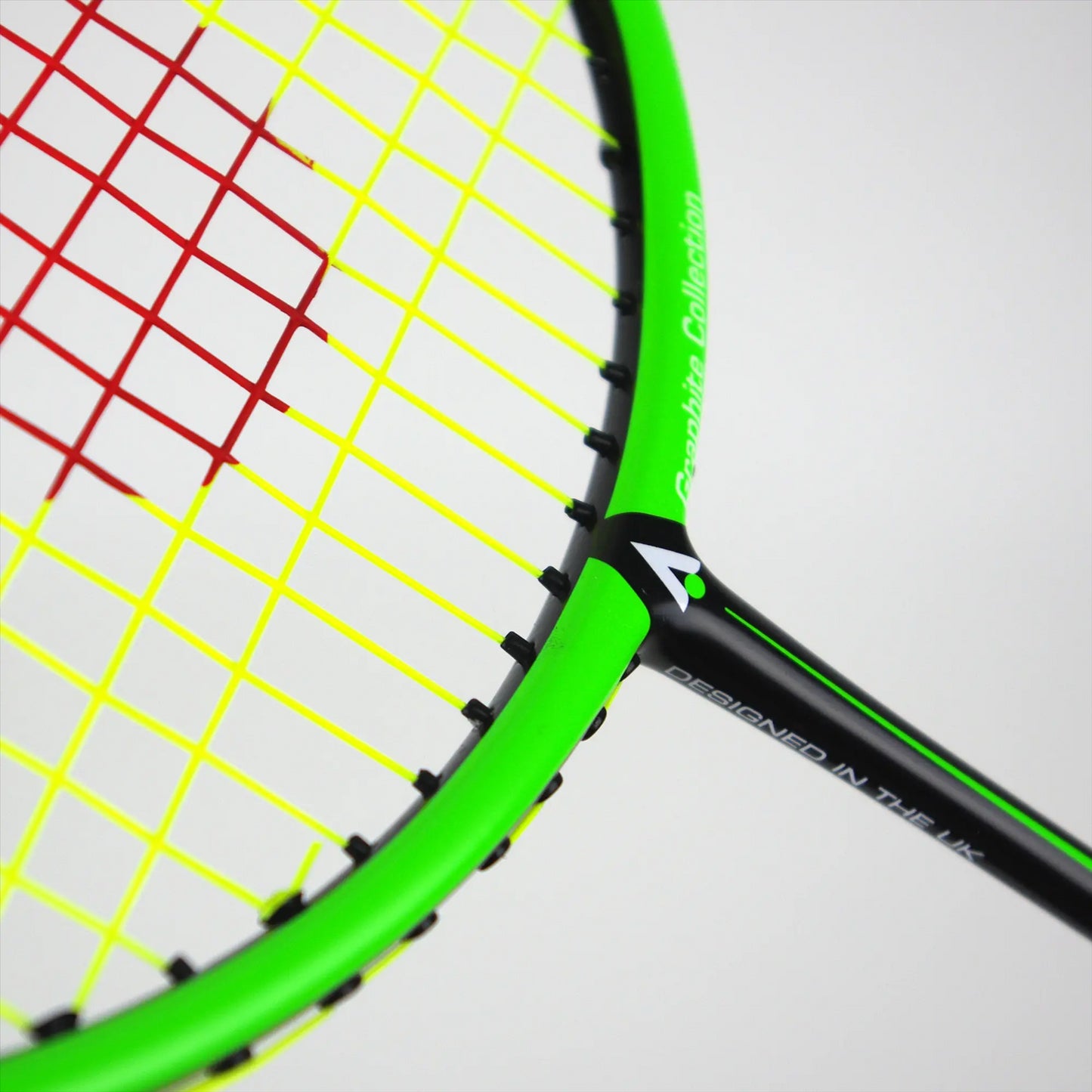 The close-up of the vibrant Karakal BZ 20 2.1 Badminton Racket in Black and Green showcases an isometric head with a bright green frame, red main strings, and yellow cross strings. Its handle features a PU super grip along with white text, indicating it was designed in the UK.