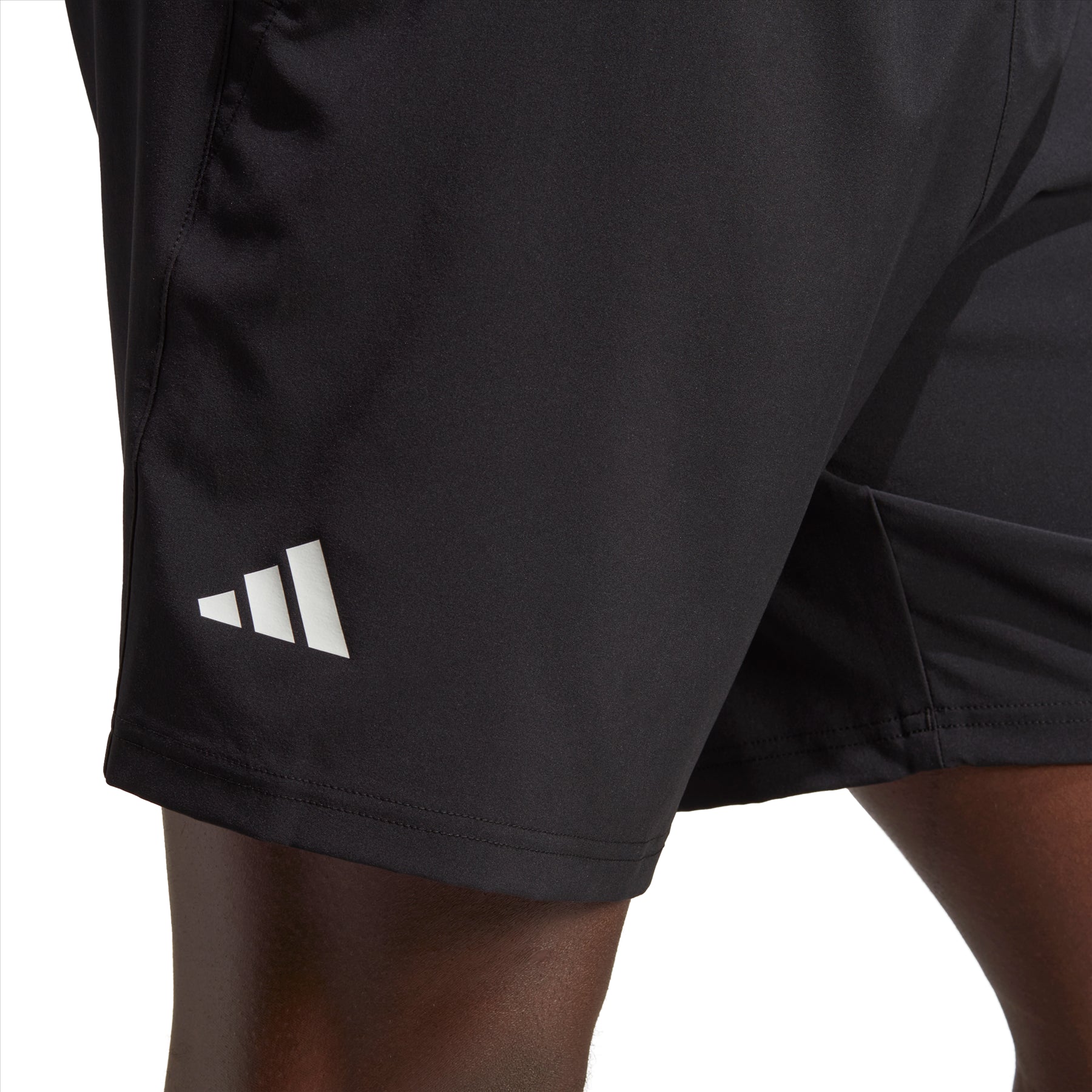 Close-up of an individual wearing the adidas Club Stretch Woven 7" Men's Badminton Shorts in black, highlighted by the distinctive white Adidas logo on the left side. Designed with AEROREADY technology, these shorts boast a sleek texture and provide comfort, as demonstrated by the visible section of their leg.