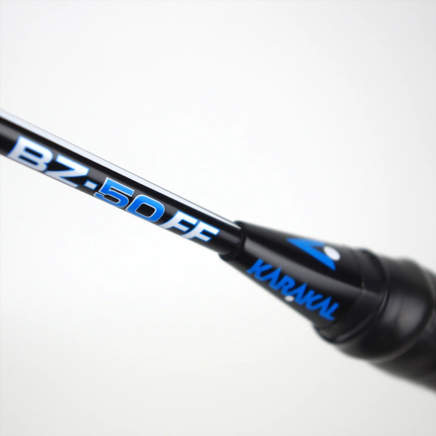 A close-up of the Karakal BZ 50 2.1 Badminton Racket in black and blue shows the brand name "Karakal" along with the model "BZ-50 FF" on its shaft. The isometric square head is designed to enhance precision, and it features construction from Karakal NEXGEN Fast Fibre Graphite, standing out against a soft, blurred gray background.