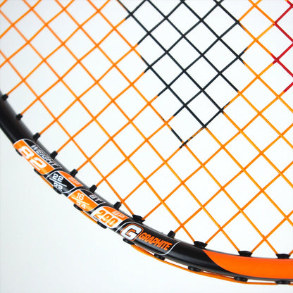 Close-up of a Karakal BZ 30 2.1 badminton racket in black and orange, showcasing its isometric head design and intricate string pattern. The branding details, including "Karakal" and various specifications, are prominently visible along the frame's side.