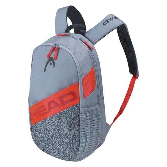 The HEAD Elite Backpack - Grey Orange, a stylish tennis bag, features the brand name prominently displayed. It includes a zipper closure, side mesh pockets, black padded shoulder straps, and a padded racket compartment. The lower front panel is decorated with a subtle graphic pattern.