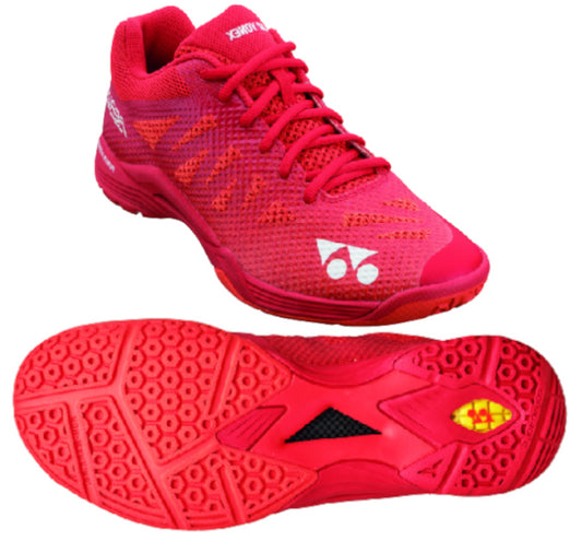 A vibrant red Yonex Power Cushion Aerus 3 men's badminton shoe is showcased from two perspectives: one side view highlighting the laces and Double-Russel Mesh design, and a bottom view displaying a textured sole featuring hexagonal patterns and a unique logo near the heel, all enhanced by Yonex's signature Power Cushion technology.