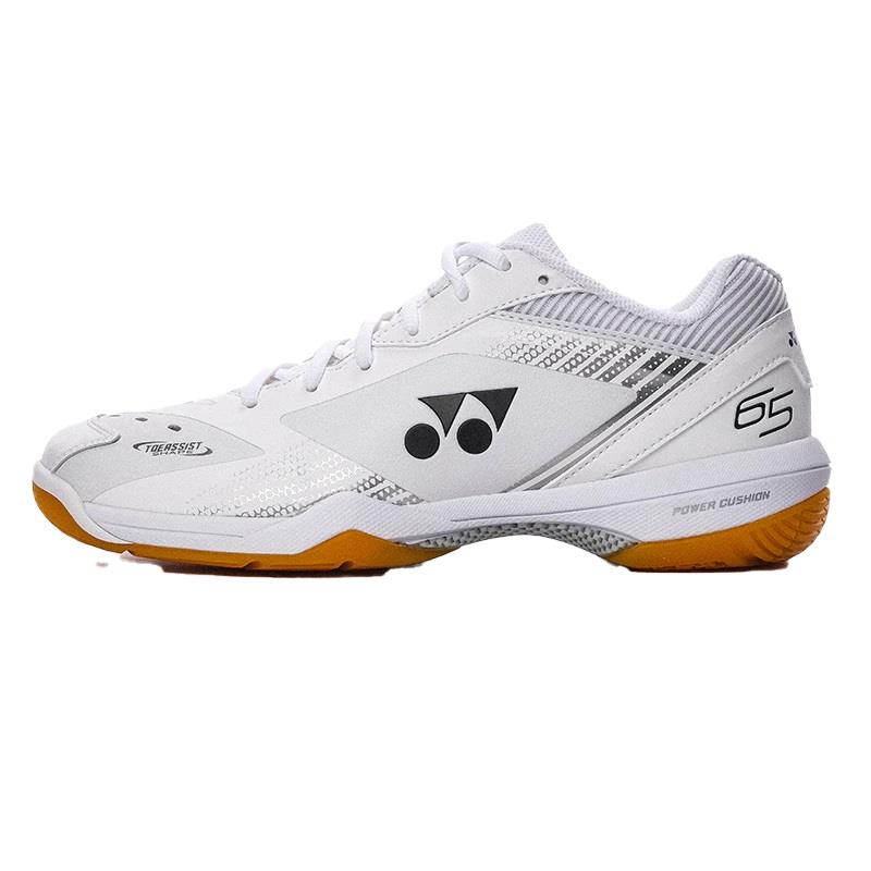 Introducing the Yonex Power Cushion 65Z3 Mens Badminton Shoes in white, showcasing a sleek low-cut design with a distinctive black brand logo and an eye-catching orange sole. These shoes ensure an ultra-comfortable fit with "65" prominently displayed on the heel and are equipped with the renowned Yonex Power Cushion technology in the midsole for superior performance.