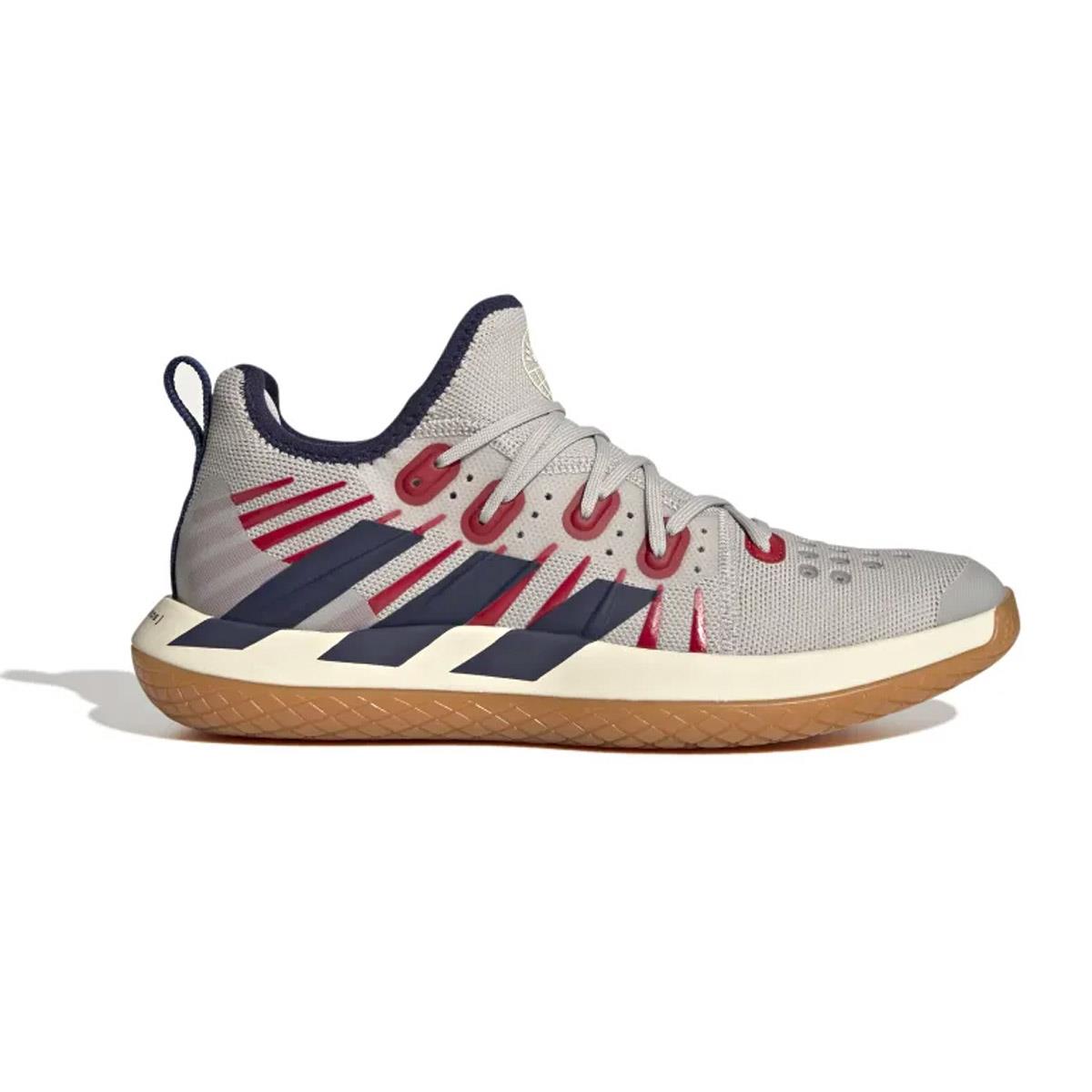 The ADIDAS Stabil Next Gen 2.0 Primeblue Men's Indoor Badminton Shoes by adidas feature a light gray upper with striking red eyelets and diagonal navy blue stripes, all set on a tan sole. Engineered for agility, these shoes incorporate BOOST technology to provide enhanced comfort, making them ideal for any indoor badminton court.