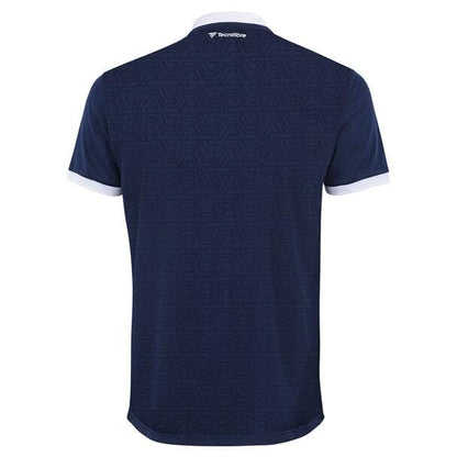 Rear perspective of the Tecnifibre Mens Team Badminton Mesh Polo Shirt in marine blue, showcasing a white collar and sleeve edges. Constructed from polyester mesh, it ensures excellent breathability. The polo sports a delicate geometric pattern along with the "Tecnifibre" logo positioned at the upper center.