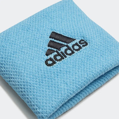 A close-up of the adidas Wristband Sweatband Small in blue showcases its textured, woven fabric made from recycled materials. The distinctive adidas logo is prominently displayed, emphasizing the brand's dedication to sustainability while providing moisture-absorbing comfort.