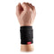 A hand adorned with the McDavid Adjustable 2-Way Adjustable Elastic Wrist Sleeve, featuring a red logo on its black design. Crafted from breathable elastic materials, the sleeve is fastened securely with a Velcro strap, providing mild compression and support to the wrist area. The skin tone of the hand is light.