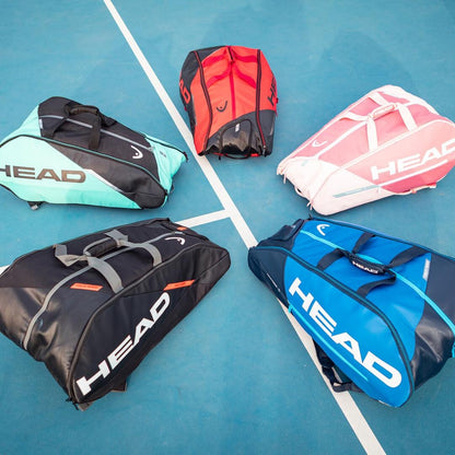 A blue court is adorned with five tennis bags in vibrant colors such as aqua, red, pink, black, and navy, all flaunting the "HEAD" branding. Notably among them is the HEAD Tour Team 9R Supercombi 9 Racket Badminton Bag in black and orange, equipped with CCT+ climate control technology. Displaying diverse shapes and adorned with multiple zippers, these bags are positioned close to the court lines.