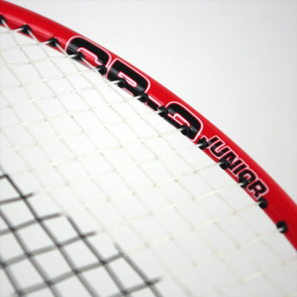 A close-up of the Karakal CB-2 2.1 Junior Badminton Racket showcases its red frame with an aluminium head and white strings, featuring "Junior" text and numeric markings in black. The focus is on the upper section of the racket set against a simple white background.