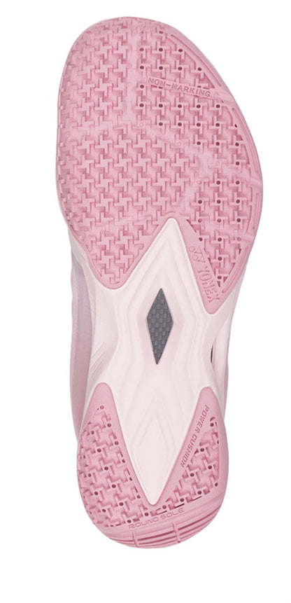 The image highlights the sole of the Yonex Power Cushion Aerus Z2 Women's Badminton Shoes in light pink and white, displaying a textured pattern. Featuring a central triangular section with a grey accent for enhanced traction, this sole is crafted from non-marking rubber and incorporates Power Cushion technology to provide reliable support during play.