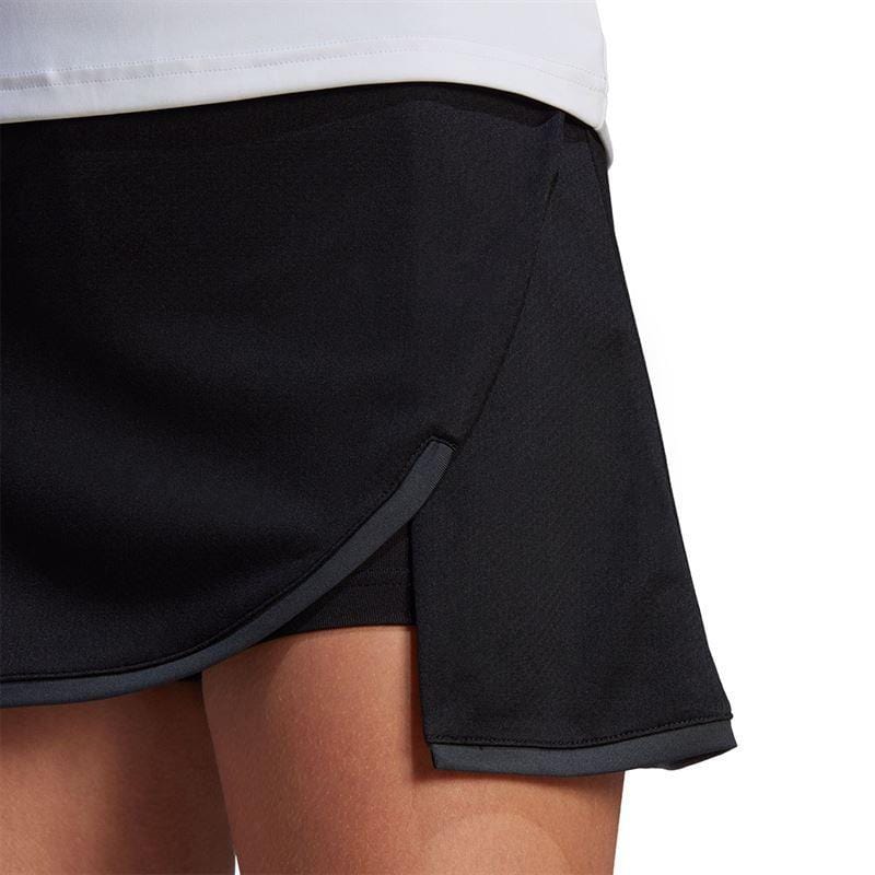 A close-up shot shows a person wearing the adidas Womens Club Badminton Skirt in black, which features a subtle front slit and a comfortable wide waistband. Paired with a white top, the image highlights the skirt's design and AEROREADY fabric texture on the lower body.