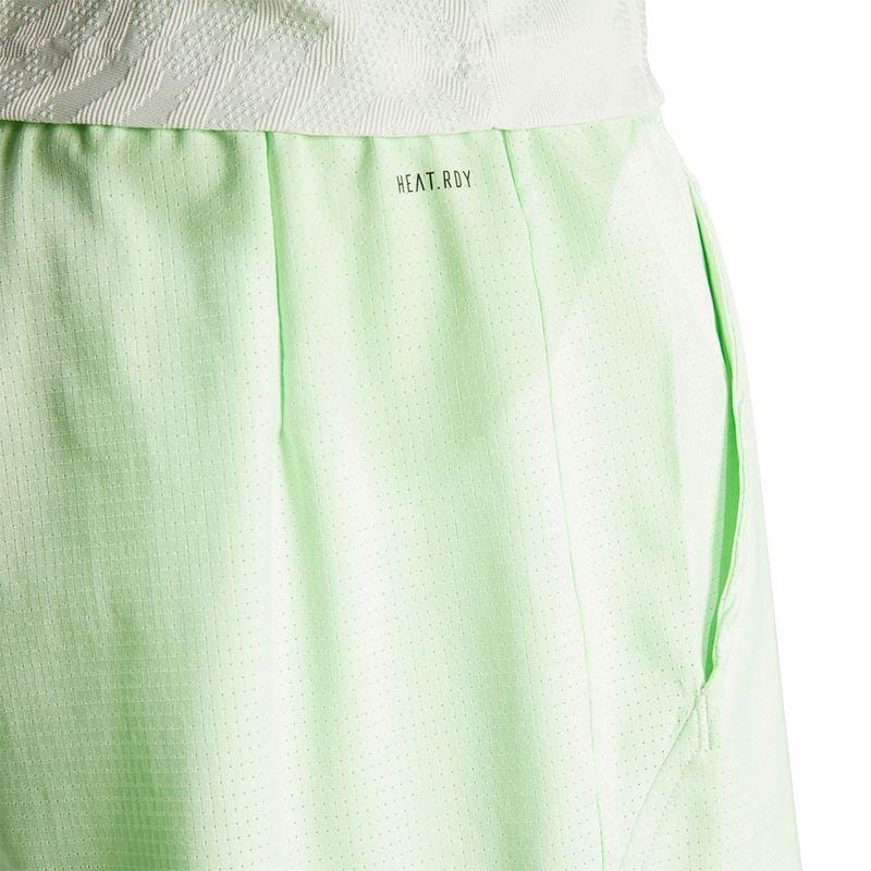 Close-up of the ADIDAS Melbourne Men's 2in1 Badminton Shorts in green, showcasing a subtle dot pattern. Made with recycled materials, these loose-fit shorts feature the "HEAT.RDY" fabric label near the waistband and are designed for comfort during physical activity.