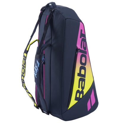 A Babolat RH6 Pure Aero Rafa II badminton bag in blue, yellow, and pink, featuring multiple compartments and shoulder straps. The design includes an insulated racket bag for protection and prominently displays the "Babolat" logo on the side.