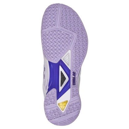 The image displays the sole of a Yonex Power Cushion Eclipsion Z3 women's badminton shoe in white and purple, featuring a blend of light purple and white rubber with a textured geometric pattern. A central purple section with a cut-out reveals a white grid, enhanced by Yonex Power Cushion technology for improved stability and includes a small yellow detail near the heel.