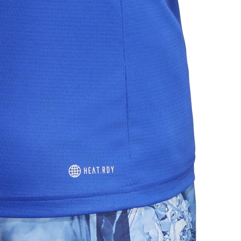 A close-up showcases the intricate fabric texture of the adidas Melbourne Mens Raglan T-Shirt - Lucid Blue, with "HEAT.RDY" prominently printed on the blue shirt, perfectly complemented by patterned blue shorts. Crafted from recycled materials, it seamlessly merges style and sustainability.