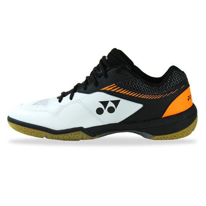 A side view of the Yonex Power Cushion 65Z2 Men's Badminton Shoes in White Orange showcases the non-marking gum sole. The shoes predominantly feature a white color scheme, accented with black and orange highlights, and display a distinctive Yonex logo. They are equipped with Power Cushion technology for comfort and 3D Power Graphite Drive for enhanced stability, while mesh detailing provides breathability.