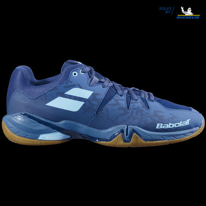 The Babolat Shadow Spirit Badminton Shoes in Dark Blue feature a textured design paired with a gum Michelin rubber sole. They prominently display the Babolat name and logo on the side, include sleek blue laces, and have "Soles by Michelin" inscribed in the top right corner.