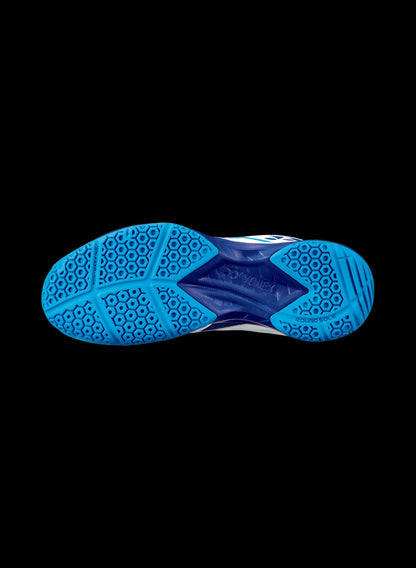 The image showcases the sole of the Yonex Power Cushion 39 Junior Badminton Shoes in a white and blue colorway, featuring a vibrant blue tread pattern with hexagonal shapes and diverse textures set against a black background. This design is enhanced by Yonex's Power Cushion technology for superior comfort and performance.