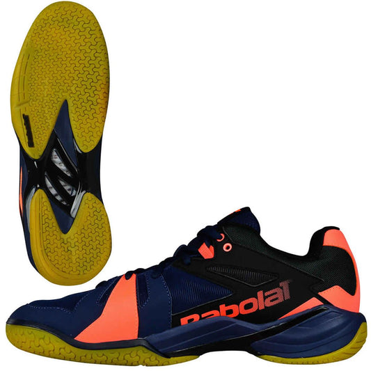 A pair of Babolat Shadow Spirit badminton shoes in a captivating navy blue and fluo orange color scheme. One shoe is presented from the side, prominently showcasing the Babolat logo, while the other emphasizes its robust grip treads with a uniquely patterned sole.