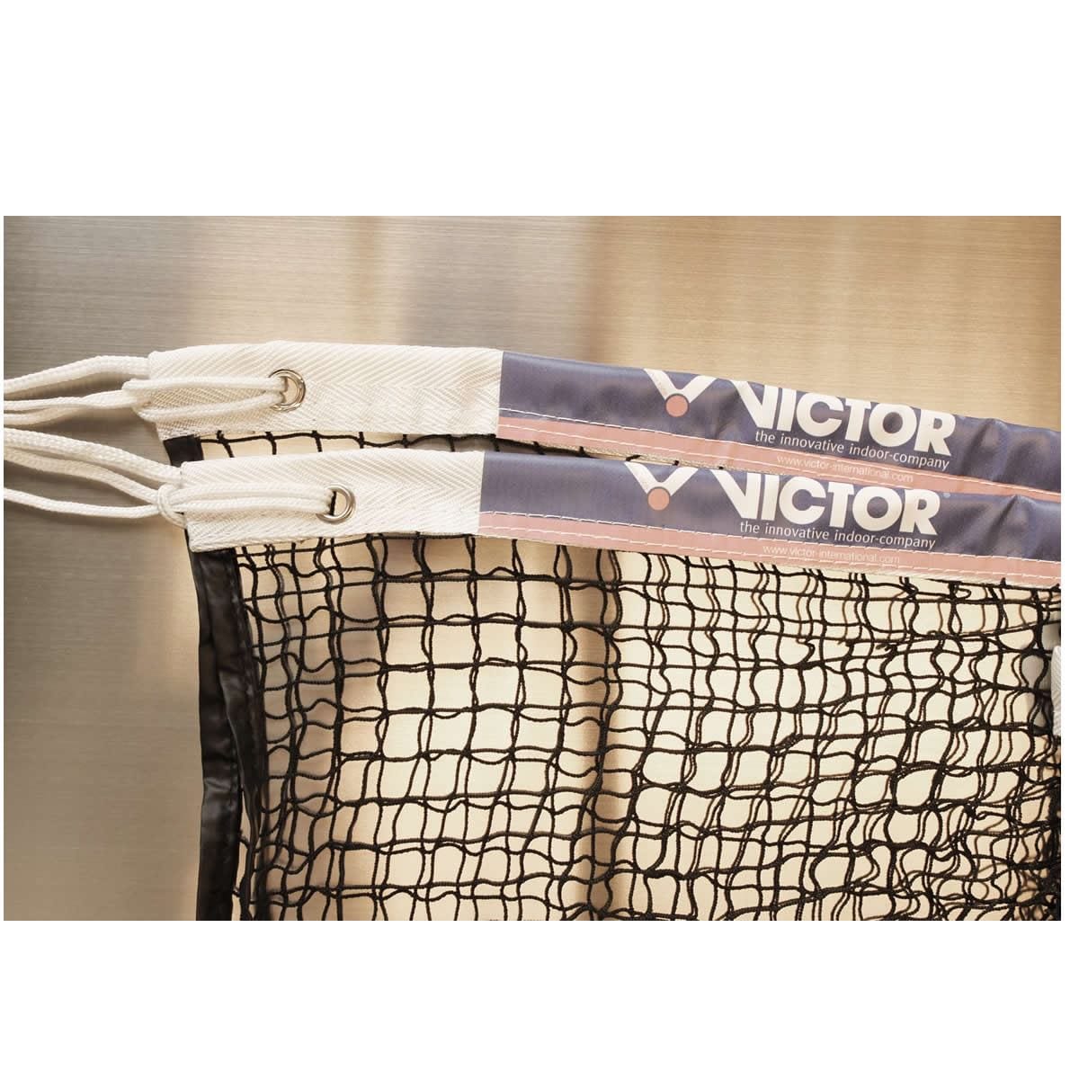 Close-up of two Victor Badminton Net A Professional - BWF approved nets hanging side by side. Each showcases a white and black mesh design with blue and beige bands at the top, labeled "Victor." Ideal for competition use, they are reinforced with durable nylon cord for added strength.