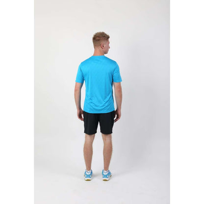 A person with short blond hair is standing and facing away from the camera, wearing an FZ Forza Byron Blue Badminton T-Shirt, which features a smart neckline. They pair it with black shorts and blue athletic shoes. The lightweight material of the shirt contrasts against the plain white background.