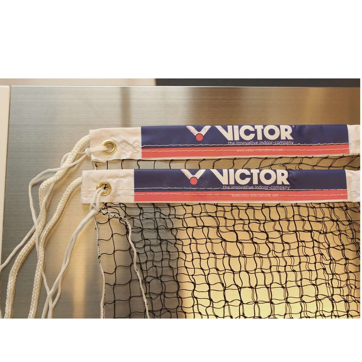 A close-up of two Victor Badminton Net B Nationals highlights the durable nylon cord design and white edges adorned with a blue, red, and white Victor logo. The nets feature white strings fastened to polyester tape along the edges and rest elegantly on a metallic surface, poised for competition.