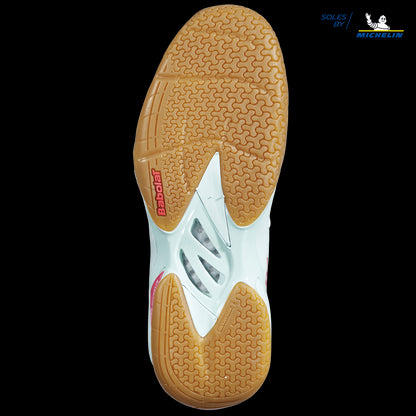 The image showcases the sole of a Babolat Shadow Spirit women's badminton shoe set against a black background. The gripsole is mostly light brown with a textured pattern designed to improve traction. The midsection features a white cutout with the "Babolat" branding visible, while the top right displays the Michelin logo.