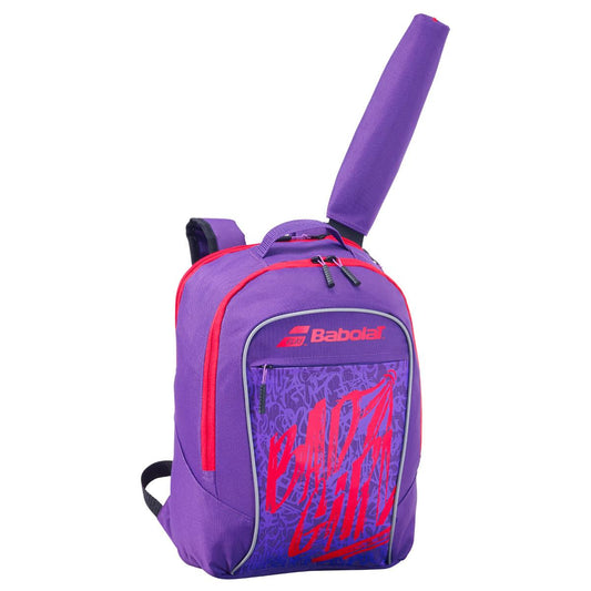 The Babolat Kids Badminton Backpack in a vibrant purple, ideal for carrying training gear, prominently features a racket handle protruding from the top. This backpack includes a zippered main compartment, a smaller front pocket adorned with red graffiti-style text, and adjustable shoulder straps for added comfort.