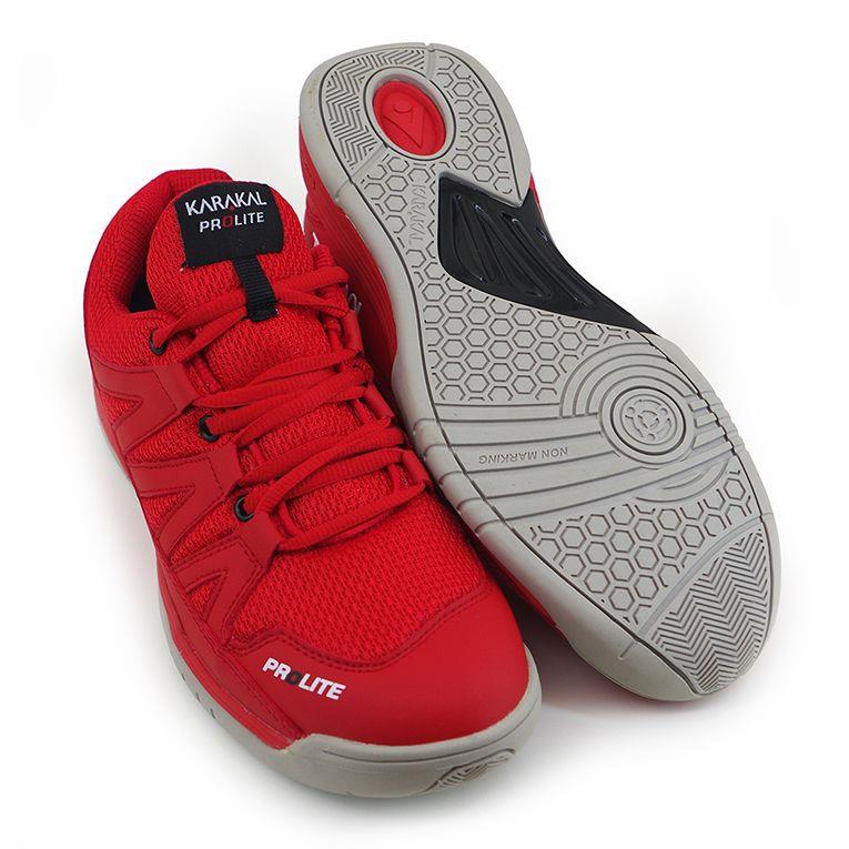 A pair of eye-catching red Karakal KF Pro Lite Men's Badminton Shoes showcases the brand name on the sides. One shoe stands upright, emphasizing its sleek design, while the other lies on its side, unveiling a textured sole and a non-marking outsole designed for optimal lateral stability.