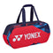 The Yonex 92231WEX Pro Tournament Bag - Scarlet features a striking geometric design in red, blue, and black. Equipped with dual handles and a zippered top, this bag is ideal for transporting sports equipment. As a professional-grade product, it prominently displays the Yonex logo on the side.