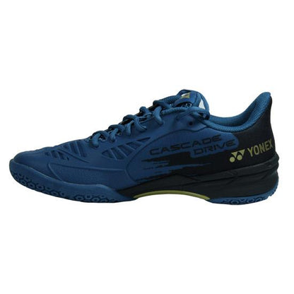 The Yonex Power Cushion Cascade Drive Badminton Shoes in teal blue, crafted by Yonex, showcase a sleek design with black accents and a yellow logo. They are equipped with a textured sole for optimal grip, superior shock absorption courtesy of the Yonex Power Cushion technology, and feature a lace-up closure to ensure a secure fit.