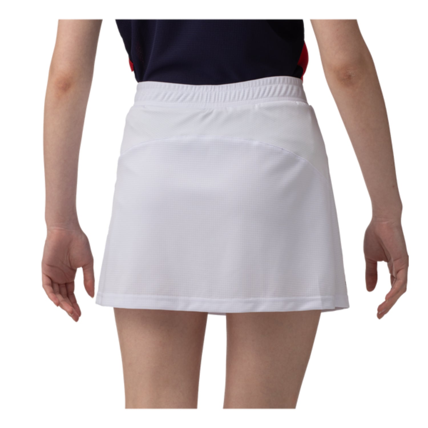 A person is seen from behind wearing the Yonex 26094 Women's Skort in white, designed with UV reduction. The knee-length skort, featuring a textured pattern, perfectly complements a dark top. Their arms are relaxed by their sides against a plain white background, highlighting this advanced technology in action.