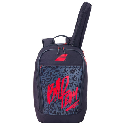 The Babolat Classic Club Badminton Backpack in black with red accents has graffiti-style text that reads "BAD TEAM" on the front pocket. Ideal for training, it offers multiple compartments, including a side pocket and a racket compartment. The main compartment is partially unzipped.