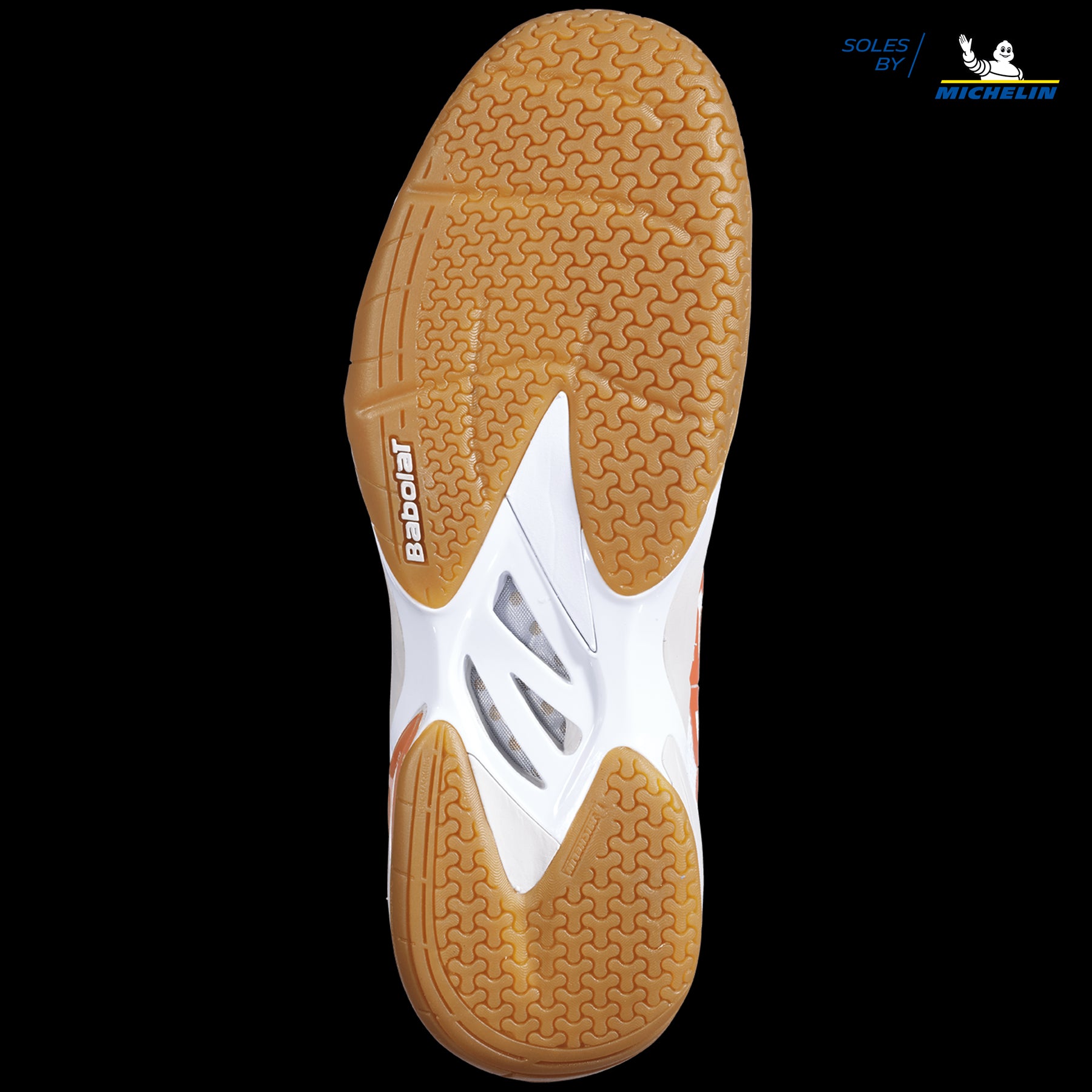 The image displays the sole of the Babolat Shadow Tour Badminton Shoes in White and Light Grey, featuring a unique textured pattern. This bi-density sole primarily showcases tan with white segments and includes the "Babolat" and "Soles by Michelin" logos, underscoring its advanced DCS technology for improved performance.