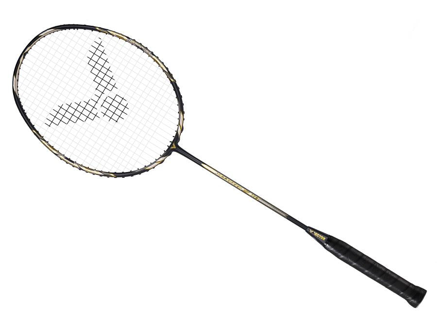 The Victor Jetspeed S10C Badminton Racket in Black Gold, expertly crafted from premium Japanese carbon fibre, boasts a striking black and gold design with the Victor logo adorning the stringbed. Positioned elegantly against a white background, its handle is wrapped in sleek black grip tape.