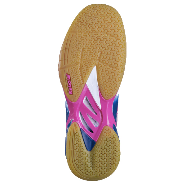 The Babolat Shadow Tour Badminton Shoes in White and Pink showcase a vibrant sneaker sole with pink, blue, and white accents. They incorporate DCS technology for improved grip with a sandy brown non-slip pattern, while the Babolat brand name is prominently displayed on the pink section, blending style with performance.