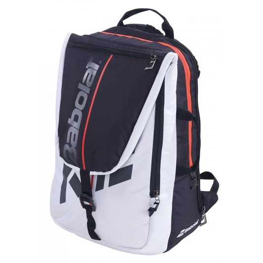 The Babolat Pure Strike Backpack - White/Black, accented with stylish red details, boasts a zippered front pocket and a spacious main compartment. The bold "Babolat" branding adorns the front flap. This versatile racket bag also features adjustable straps and a top handle for convenient carrying.