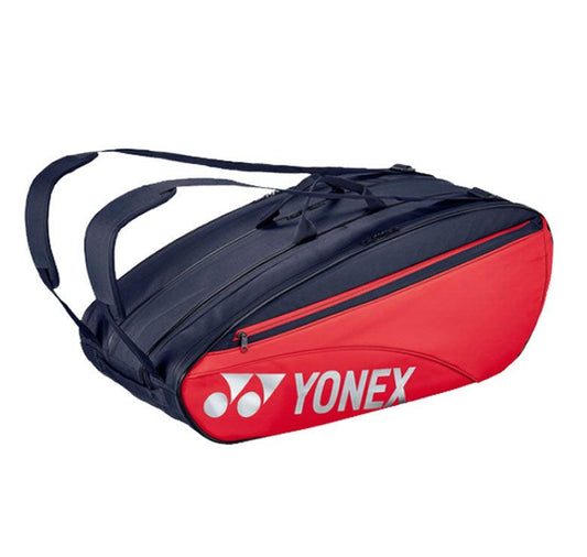 Introducing the Yonex 42329EX 9 Piece Racket Bag - Scarlet, showcasing striking red and navy accents. This bag is designed with ample storage space, multiple zippered compartments, and adjustable shoulder straps for convenience. The distinctive Yonex logo is prominently displayed on the side.