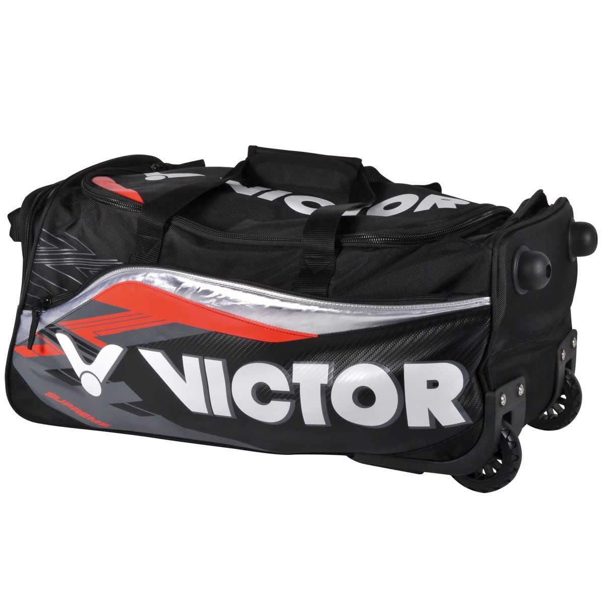 The Victor Multi Sportbag BG9712 Large Travel Badminton Bag features a sleek design with "Victor" prominently displayed in white letters on a black background. Enhanced with red and silver accents, this versatile duffle bag includes sturdy wheels for effortless transportation, offering both durability and a sporty aesthetic that make it ideal for any trip.